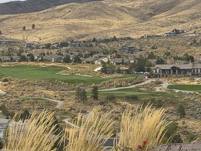 Somersett's golf course greens below homes and golden hills, with ornamental grasses and red roses in the foreground.
