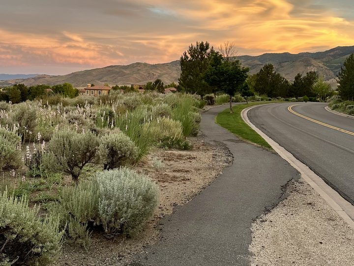 A paved Somersett trail curving beside the road through sagebrush, toward the foothills.